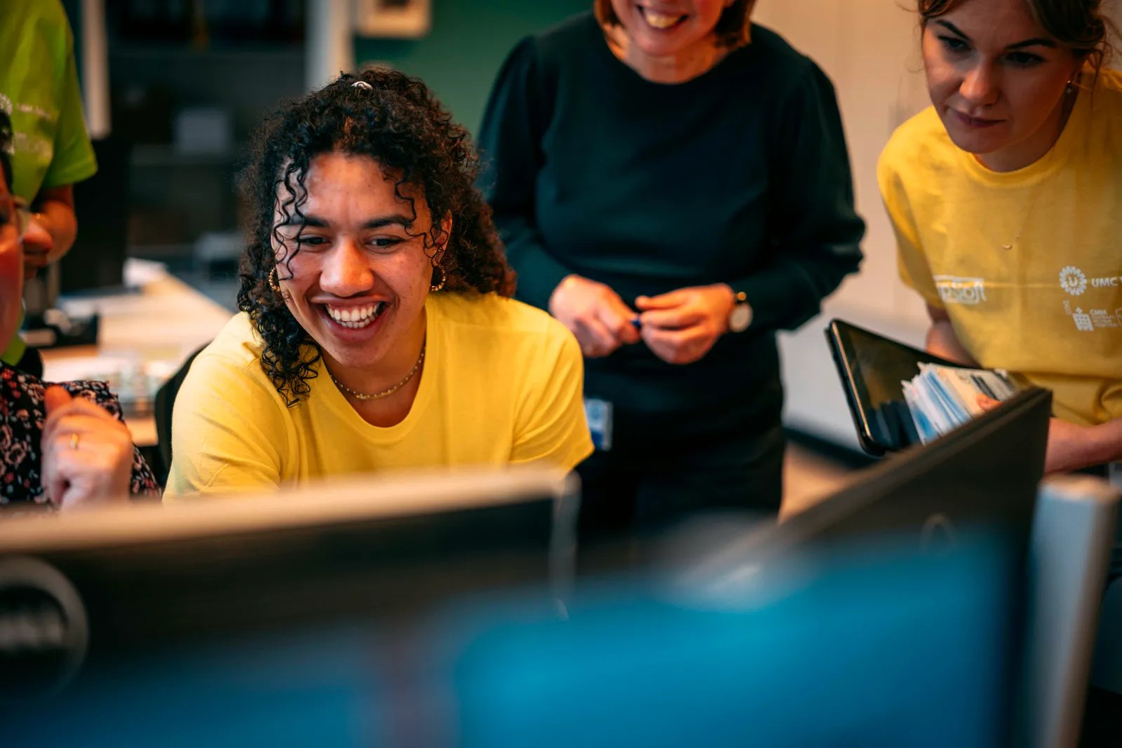 Lachende Young KINASE-medewerker achter de computer op de werkvloer