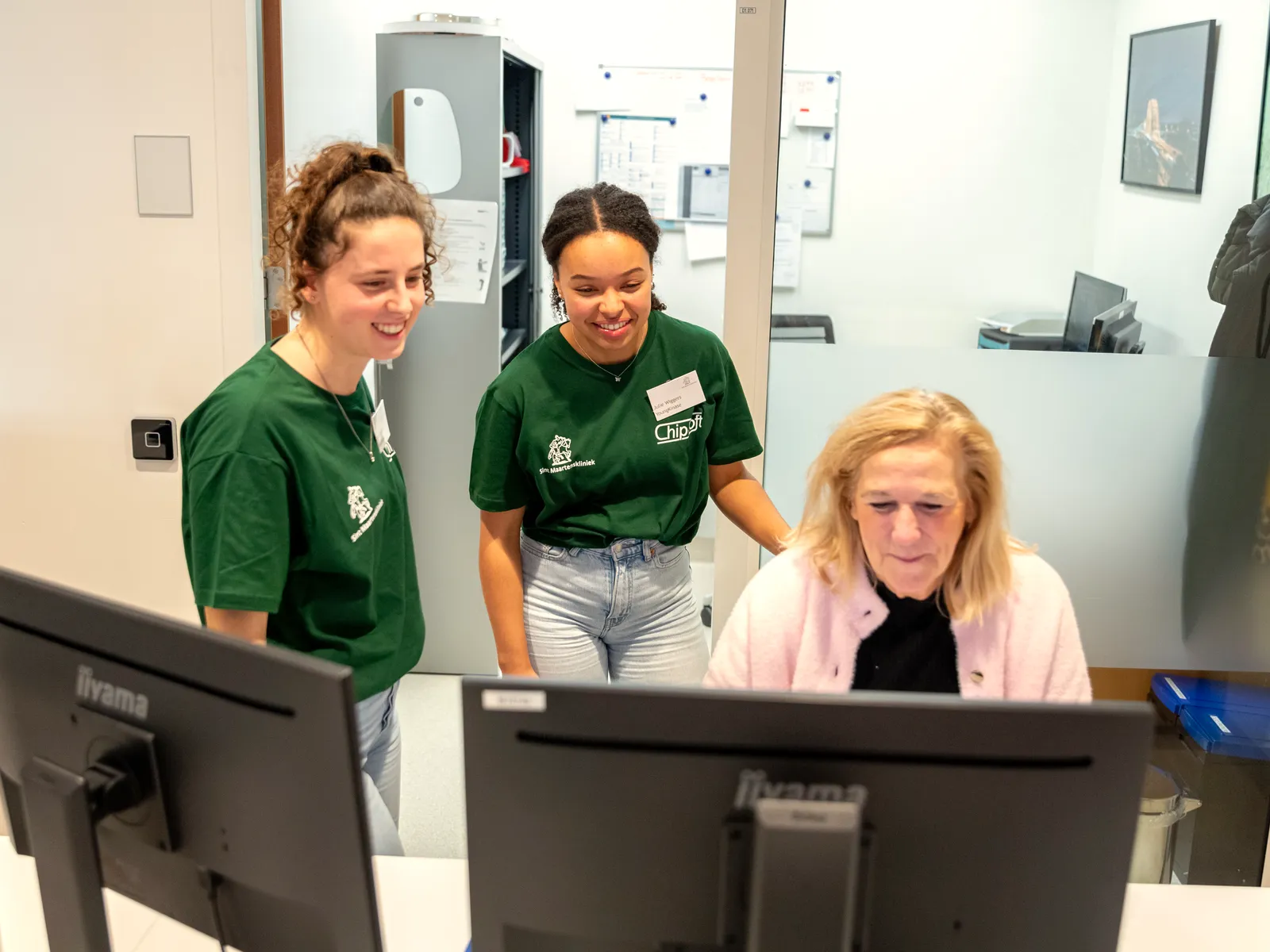Twee Young KINASE-uitzendkrachten helpen een zorgmedewerker achter de computer